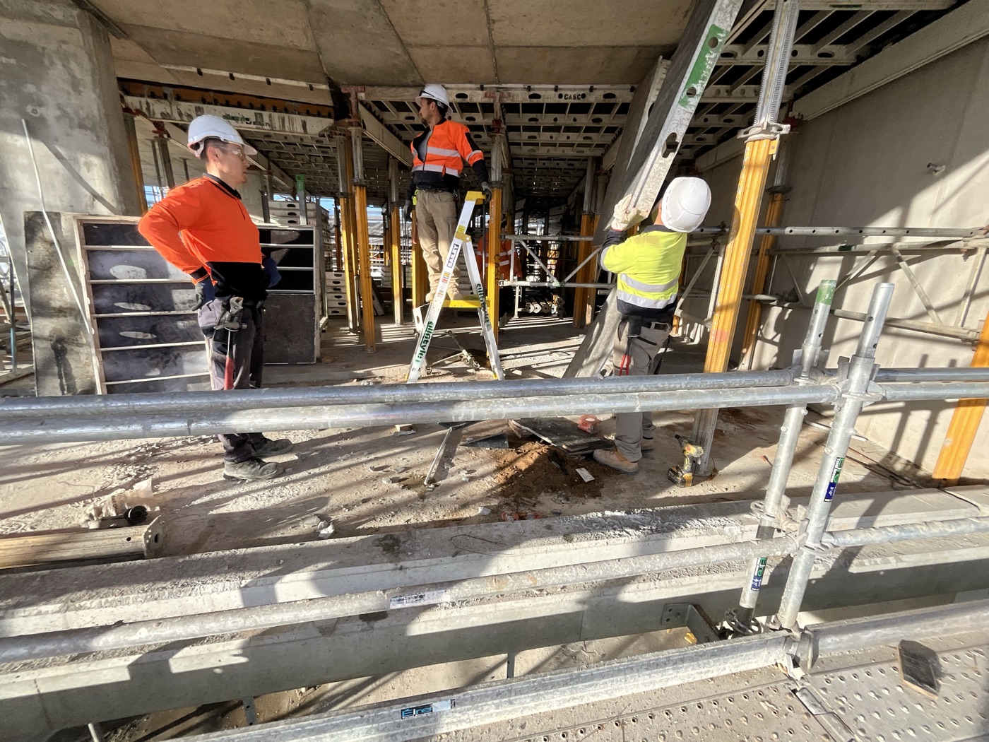 Three Togtuun crew members in full PPE — hard hats, safety glasses and high-visibility workwear — working beneath a formwork deck