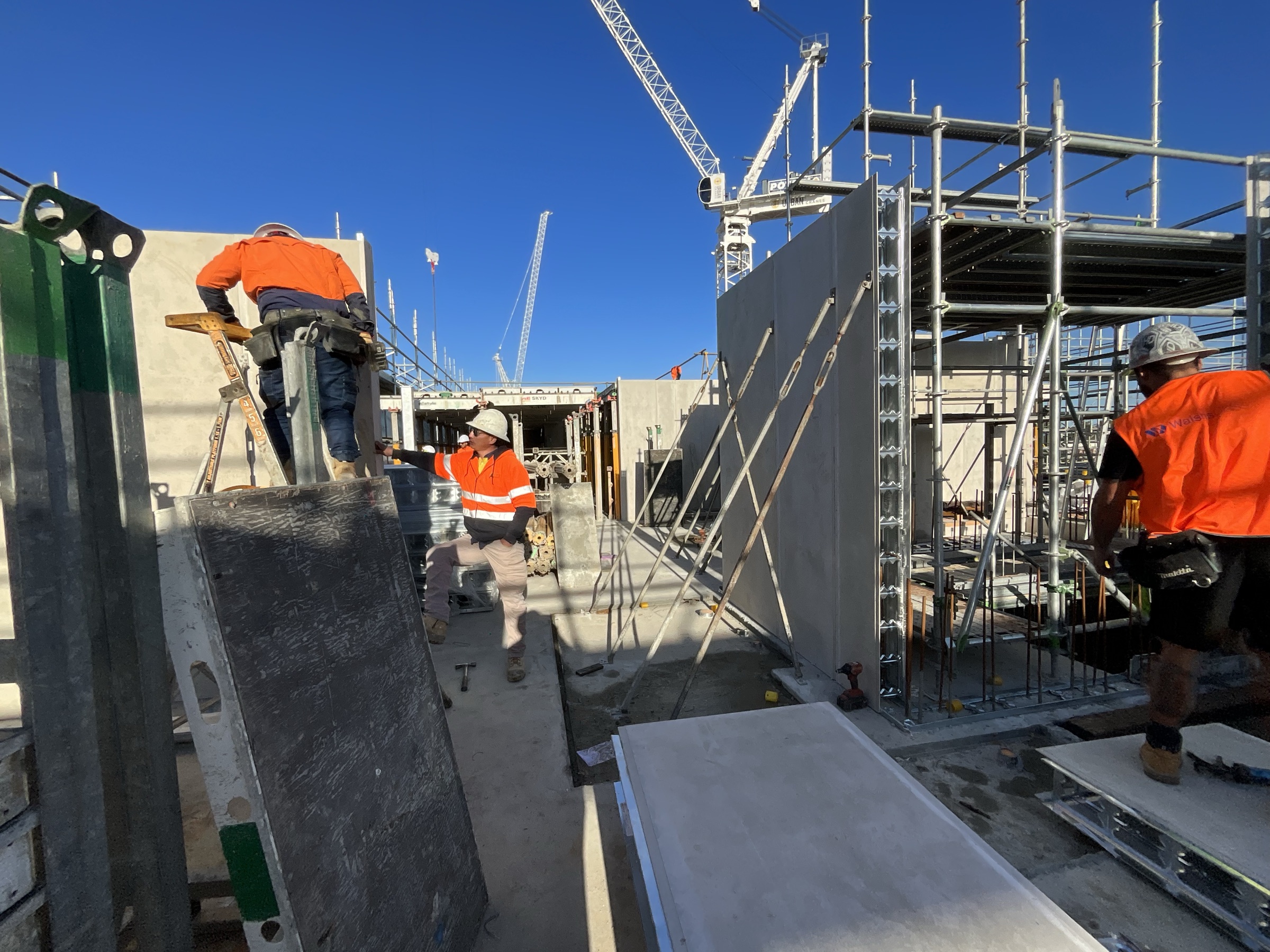 Togtuun crew in full PPE — hard hats, safety glasses and high-visibility workwear — installing precast panels beneath tower cranes on a Perth construction site